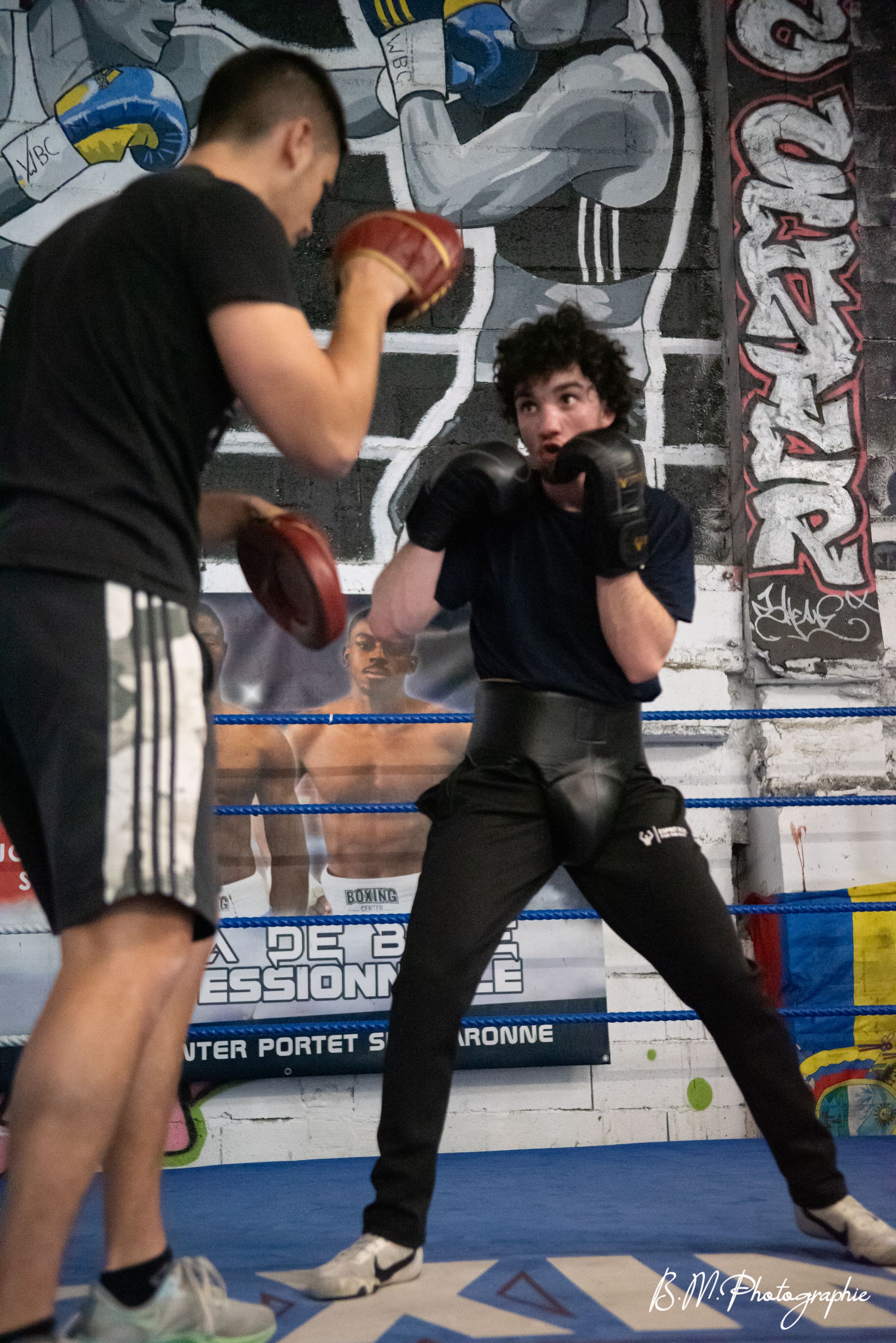 Un boxeur en garde face à un coach qui tient les pattes d’ours, dans le ring.