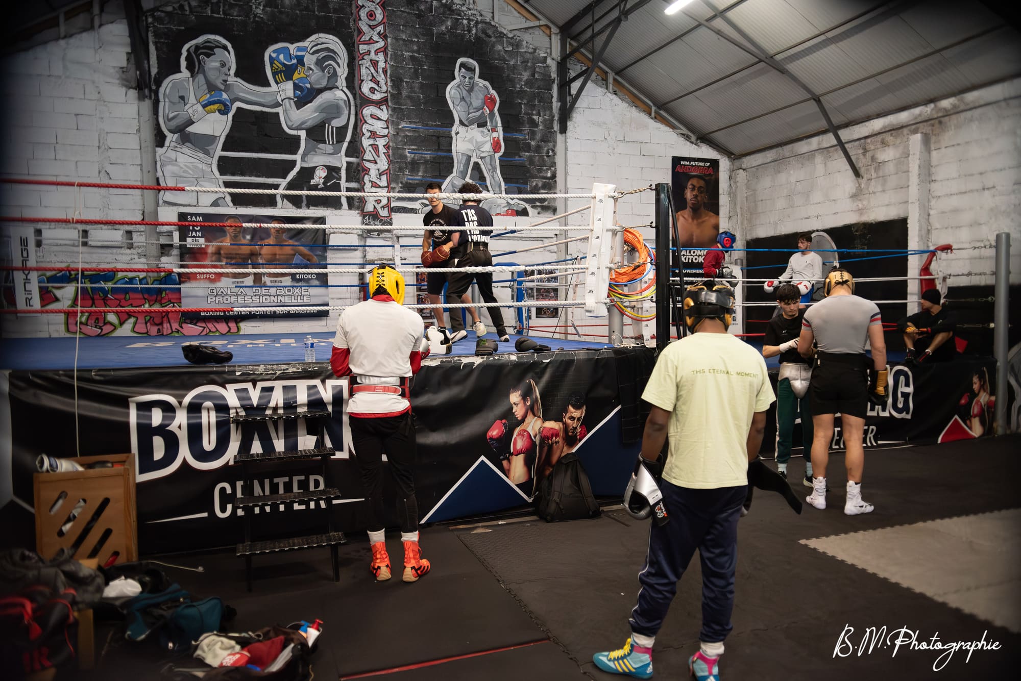 Vue large de la salle pendant un cours collectif : plusieurs pratiquants autour et sur le ring.