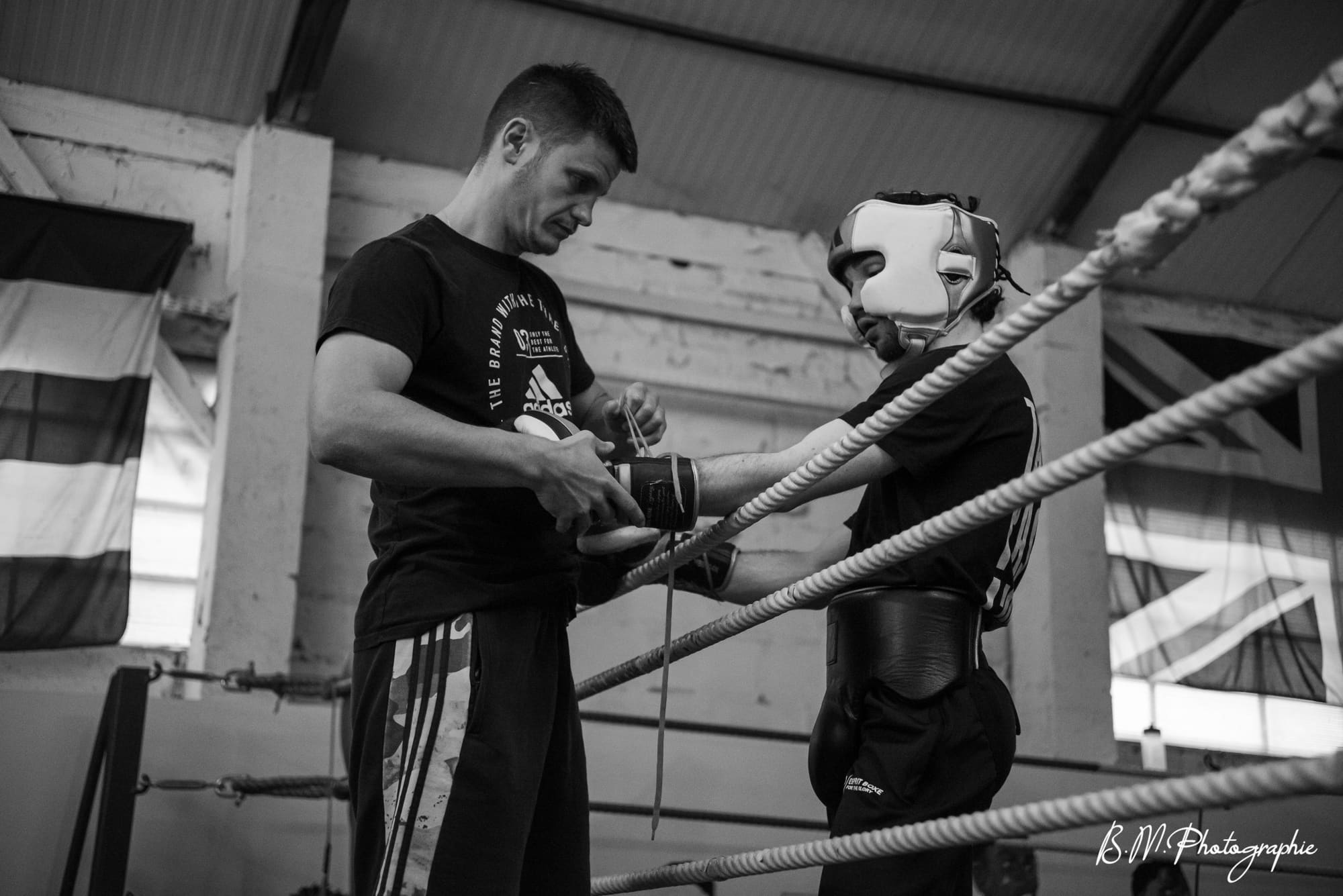 Un coach ajuste les gants d’un boxeur casqué avant de monter sur le ring.
