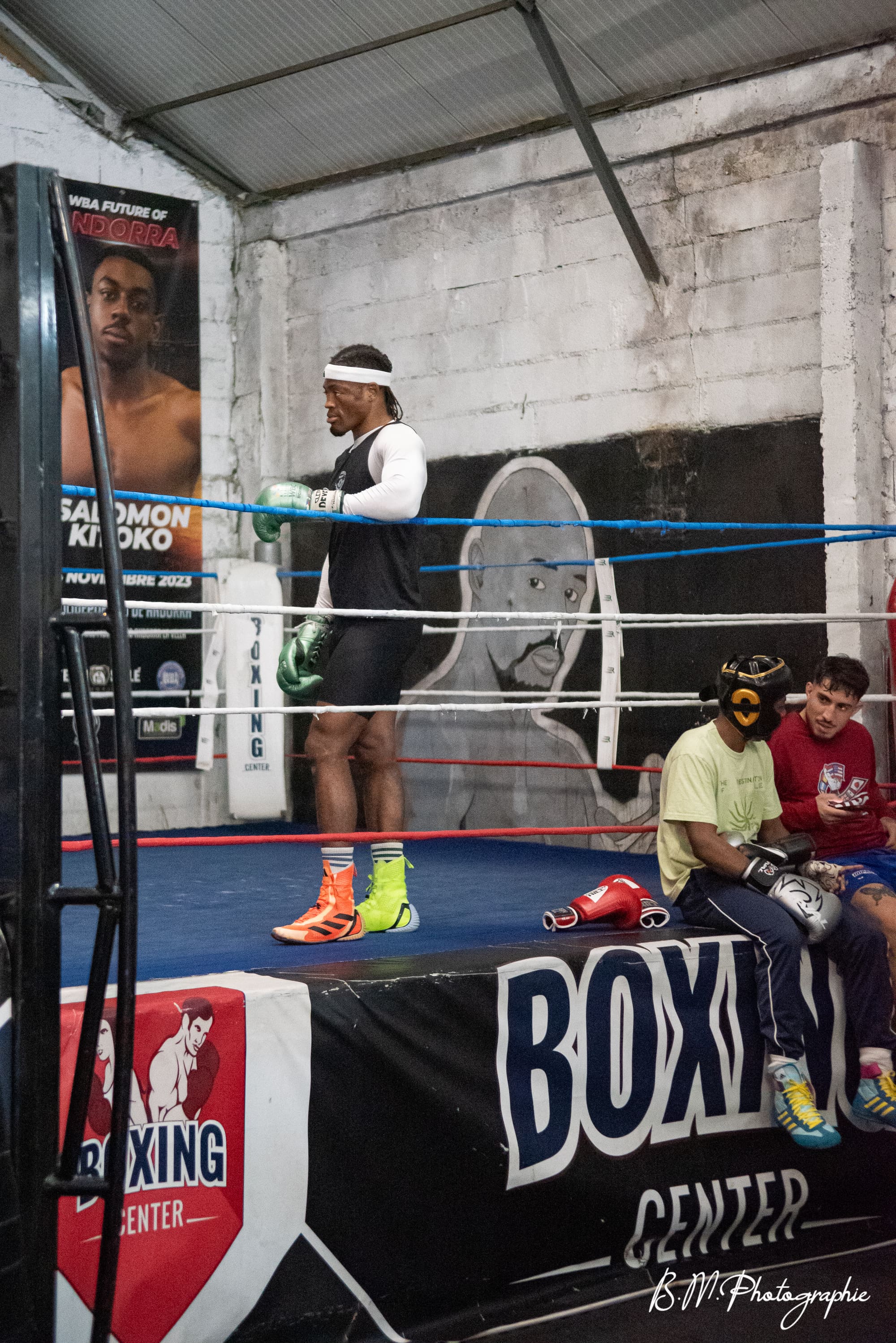 Un boxeur s’entraîne dans le ring pendant que d’autres pratiquants observent depuis le bord.